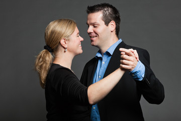 Stylish happy young couple dancing. Studio shot against grey.