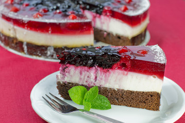 Slice of  gelatine forest fruit cake on a plate, red background