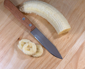 sliced banana with knife on wooden background, close-up