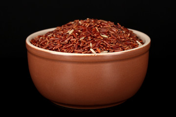 Red rice in brown bowl isolated on black