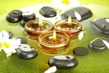 spa stones with flowers and candles in water on plate