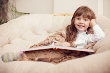 beauty child in shawl reading a book while lying on the couch