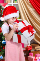 Fototapeta na wymiar A little girl opens a gift in festively decorated room