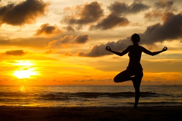 Young woman practicing yoga by the sea at sunset.