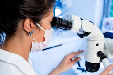 A woman in a dental practice looks in special a microscope