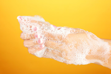 Woman's hands in soapsuds, on orange background close-up