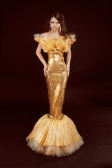 Fototapeta premium Young brunette lady in golden gorgeous dress posing on black bac