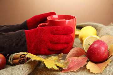 hands holding cup of hot drink and autumn leaves,