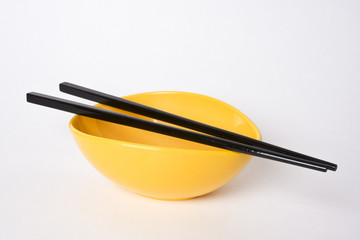 Chopsticks on an empty yellow bowl with white background