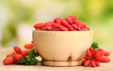 ripe barberries in wooden bowl with green leaves, on table