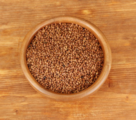 Raw buckwheat in wooden bowl on wooden background