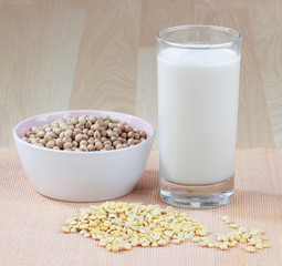 A glass of soy milk with a bowl of raw soybean and seed