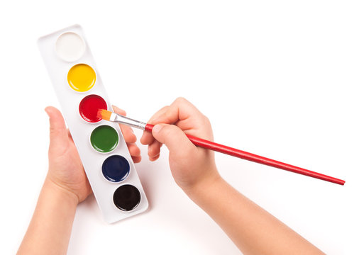 child's hand paints with watercolors and brush
