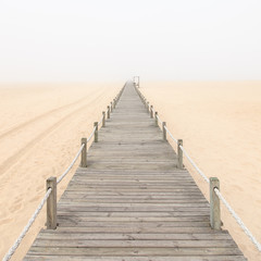 Obraz premium Wooden footbridge on a foggy sand beach background. Portugal.