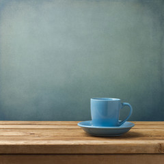 Blue coffee cup on wooden table over blue grunge background © maglara