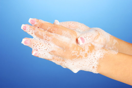 Woman's hands in soapsuds, on blue background close-up