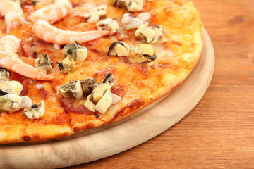Delicious pizza with seafood on stand on wooden background