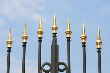 Wrought iron spikes of a gate, with a blue sky background
