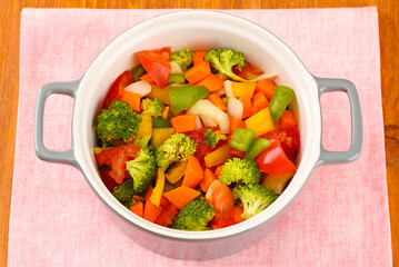 Vegetable stew in gray pot on color napkin on wooden background