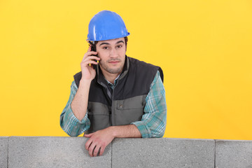 Builder stood by unfinished wall making telephone call