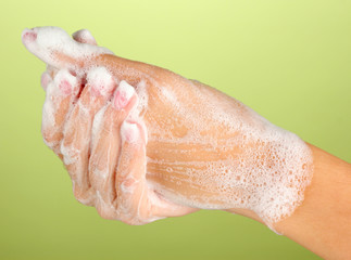 Fototapeta premium Woman's hands in soapsuds, on green background close-up