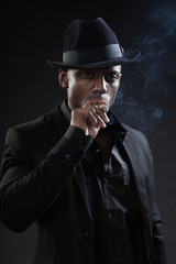 Black man wearing suit and hat gangster style smoking cigar.