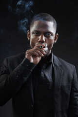 Black man wearing suit gangster style smoking cigar. Studio shot