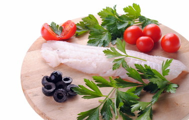 cod steak with tomatoes olives and parsley  on a wooden board