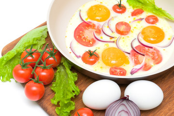 Fried eggs in a frying pan and vegetables on the cutting board