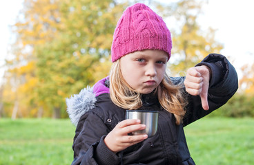 little girl drinks tea in park and showing thumbs down