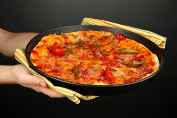 hands holding pepperoni pizza in pan on grey background