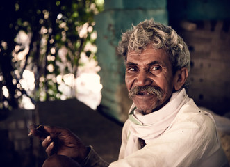 Portrait of an Indian old villager man smiling while smoking bidi. - obrazy, fototapety, plakaty