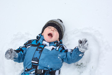 Adorable toddler boy making angel on snow