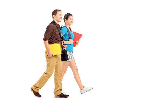 Full Length Portrait Of A Two Students Holding Books And Walking