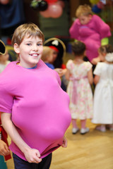 Smiling boy with balloons under pink shirt at children party.