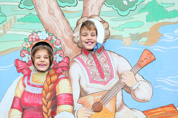 Smiling girl and boy stuck heads in plywood scenery at fair.