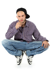 Young rapper in jeans and plaid shirt squatting isolated