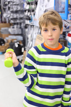 Boy in striped sweater holds small light green dumbbell in shop