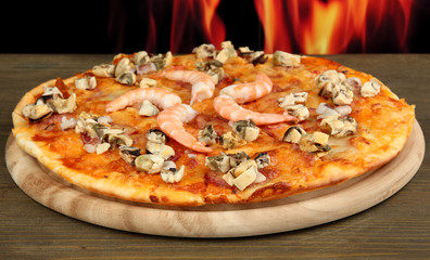 Delicious pizza with seafood on stand on flame background