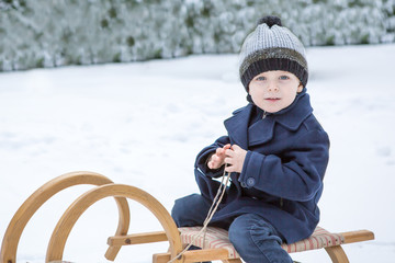 Lovely little boy on ancient sledge on winter day