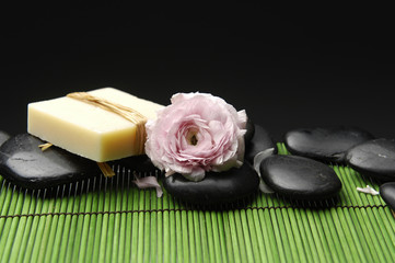 Black stones and ranunculus flower and soap in green mat