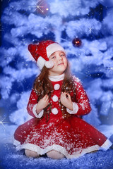 a little girl dressed as Santa Claus under the Christmas tree