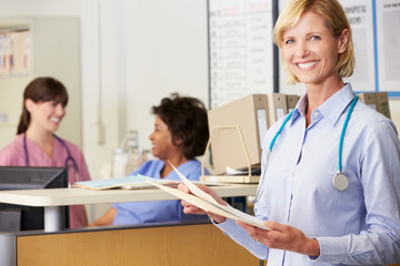 Female Doctor Reading Patient Notes At Nurses Station
