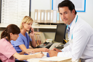 Fototapeta premium Doctor With Two Nurses Working At Nurses Station