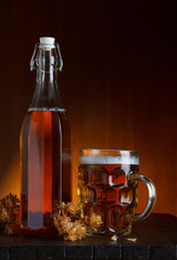 Glass of beer and bottle with hop on wooden table still life