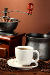 Coffee grinder, turk and cup of coffee on brown background