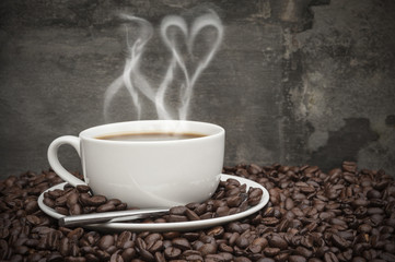 Hot coffee with heart shaped smoke, surrounded by coffee beans i