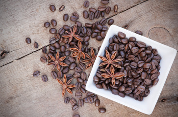 Coffee beans and star anise in a white bowl on wooden background
