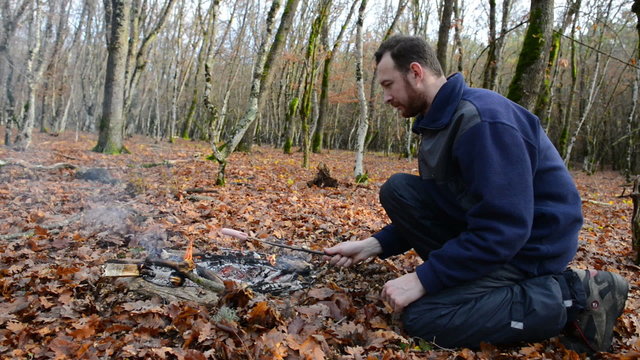 A man frying sausage on the firewood