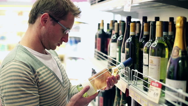 Young man choosing wine in the shop, steadycam shot